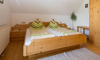 A cozy bedroom with a double bed and wooden furniture. The pillows have a green striped pattern and there is a small plant in the corner.