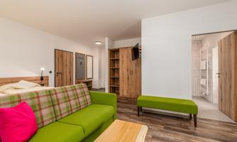 A modern living room with a green sofa and a wooden tray. In the background, shelves and a door to a bathroom are visible.