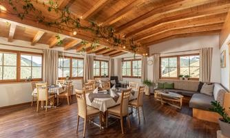 A bright and inviting dining room with wooden ceilings and large windows. There are tables and chairs as well as a cozy seating area.