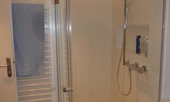 A modern bathroom with a shower cabin and a bathtub. A towel is hanging on the wall and there is a radiator.