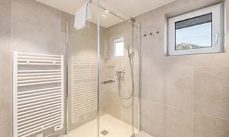A modern bathroom with a glass shower. On the wall, there is a towel dryer and a window for natural light.