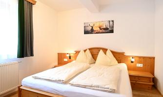 A cozy bedroom with two single beds and wooden details. On the wall hangs a picture of a deer in nature.