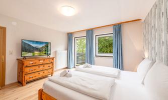 A bright bedroom with two single beds and a wooden wardrobe. Large windows offer a view of nature and let in plenty of light.
