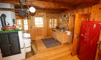 A rustic wooden kitchen with a red refrigerator and a stove. The room has large windows and a warm, inviting character.