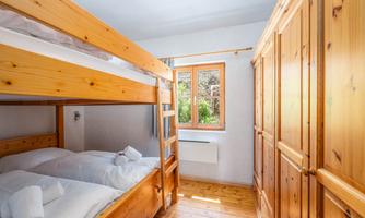 A cozy bedroom with a bunk bed and a single bed. The window provides a lot of daylight and offers a view outside.