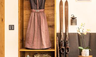 A traditional dirndl hangs on a wooden shelf, surrounded by skis and rustic decor. The room has a cozy atmosphere with natural wood and stylish accessories.