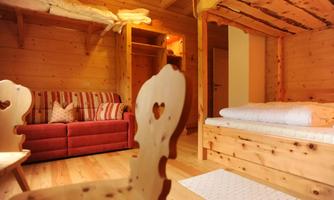 A cozy room with wooden furniture and two bunk beds. The room is bright and welcoming, with a comfortable sofa and rustic chairs.