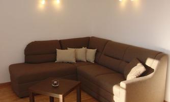 A cozy living room with a brown sofa and a table. The walls are white, and there is soft lighting.