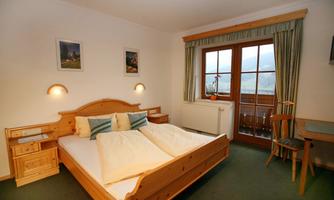 A cozy bedroom with a double bed and wooden furniture. Large windows let in plenty of daylight and provide a view outside.