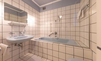 A bathroom with bright tiles and a bathtub. A sink and a mirror are also available.