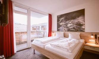 A modern hotel room with two single beds. Large windows with views of the balcony and red curtains create an inviting atmosphere.