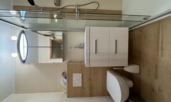 A modern bathroom with a shower, a sink, and a toilet. The walls are light and the furnishings are made of wood and white.