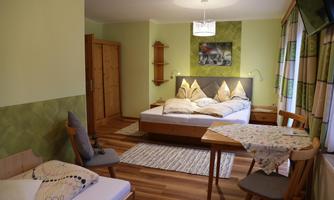 A cozy room with two beds and wooden furniture. The walls are painted in soft green tones, and there is a small seating area.