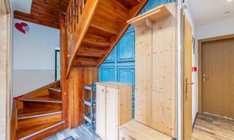 A bright hallway with a wooden staircase and a blue wardrobe. There is a shoe cabinet and a small rug in the entrance area.