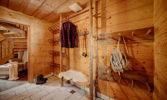 A cozy room with wooden paneling, equipped with coat hooks. Shoes are lying on the floor and a seating area is visible.