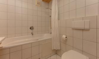 A simple bathroom with tiles, bathtub, and shower. There is a toilet and a towel rack on the wall.