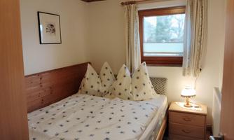 A cozy bedroom with a double bed and two nightstands. The room has large windows with curtains and a calming atmosphere.