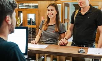 A reception desk in a hotel with an employee and two guests. The two guests appear friendly and seem to be checking in.