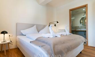 A modern bedroom with a large bed and two artistically folded towels. The room has light walls and wooden flooring, as well as a pleasant atmosphere.