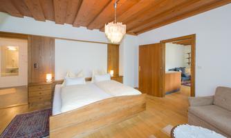 A cozy bedroom with a large wooden bed and two nightstands. The room is bright and modern, with wooden ceilings and a small seating area.