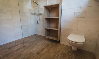 A modern bathroom with a shower and a simple shelf. The floor is designed with wooden tiles, and there is a toilet in the corner.