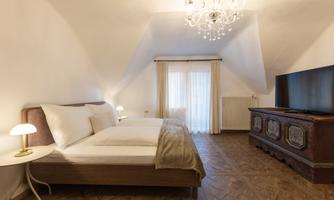 A cozy bedroom with two beds and an elegant chandelier. A large television and a bay window provide light and ambiance.