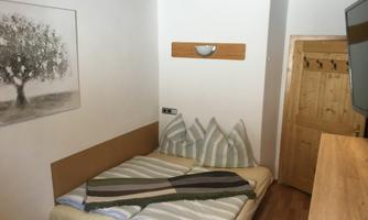 A simple room with a double bed and striped bedding. A picture of a tree hangs on the wall, and there is a television as well as a wardrobe.