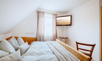 A cozy bedroom with a large bed and many pillows. A television is hung on the wall, and a window provides daylight.