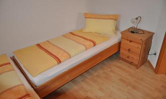 A simple bedroom with two single beds and yellow bedspreads. Next to the beds is a nightstand with a lamp.