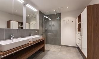 A modern bathroom with a walk-in shower and two sinks. The walls are brightly tiled, and there is plenty of natural light.