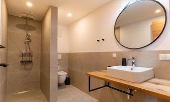 A modern bathroom with a shower and a round mirror. The walls are in neutral tones and there is a wooden panel with a sink.