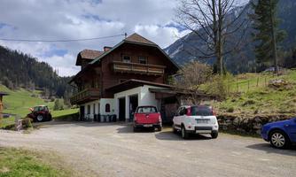 A traditional wooden house in a picturesque mountainous landscape. Several cars are parked along the road in front of the house.