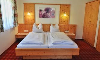 A cozy bedroom with two single beds and wooden paneling. The walls are light, and there is a small floral print above the bed.