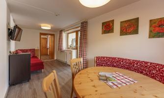 A cozy living room with a round wooden table and chairs. Pictures of red poppies are hanging on the wall, and there is a red sofa.