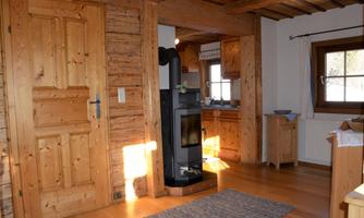 A cozy room with wooden paneling and a wood stove. The windows let in plenty of daylight and create an inviting atmosphere.