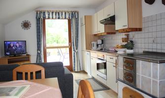 A cozy living kitchen with a dining table and a television. The windows let in a lot of light and offer a view outside.