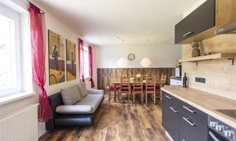 A modern kitchen with a dining area and a cozy sofa. The walls are decorated with pictures, and the wood design creates a warm atmosphere.