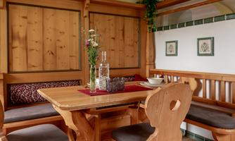 A cozy dining area with wooden furniture and warm lighting. The table is set, and there are flowers in a glass vase.