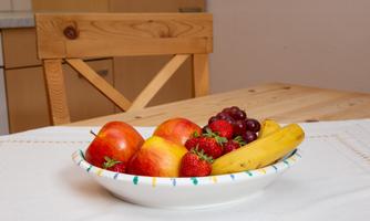 A bowl of fresh fruit is on the table. Inside it are apples, strawberries, grapes, and a banana.