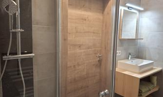 A modern bathroom with a glass shower and a wooden door. There is a sink and a large mirror on the wall.