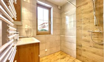 A modern bathroom with wooden details and a large window. The shower is open and there is a vanity with a mirror.