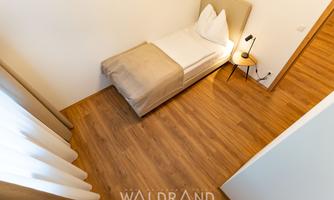 A simple room with a single bed and a nightstand. The floor is wooden and there are bright curtains.