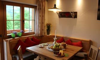 A cozy dining area with wooden furniture and red cushions. The window offers a view of the green landscape outside.