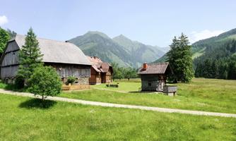 A picturesque landscape with traditional wooden houses and gentle hills. In the background, majestic mountains rise under a clear sky.
