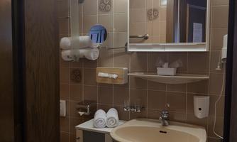 A small bathroom with a washbasin, mirror, and shelves. There are clean towels and basic hygiene items.