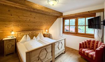 A cozy bedroom with wooden paneling and two beds. There is a television and a red armchair next to the window.