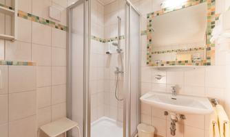 A modern bathroom with a shower cubicle and a sink. The walls are tiled and there is a mirror above the sink.