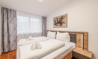 A cozy bedroom with a double bed and fresh bedding. Large windows provide plenty of daylight and a bright, inviting atmosphere.