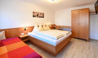 A cozy bedroom with a double bed and a single bed. The wooden details and soft lighting create a warm atmosphere.