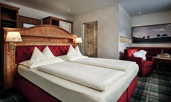 A cozy hotel room with a large double bed and red furniture. The walls are bright and the decor feels modern and inviting.